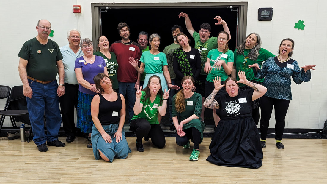 Photograph of a group of people. Most of them are making silly faces and some are striking funny poses. A lot of them are wearing green for St. Patrick's Day. They're in front of a white wall and an open double doorway. 